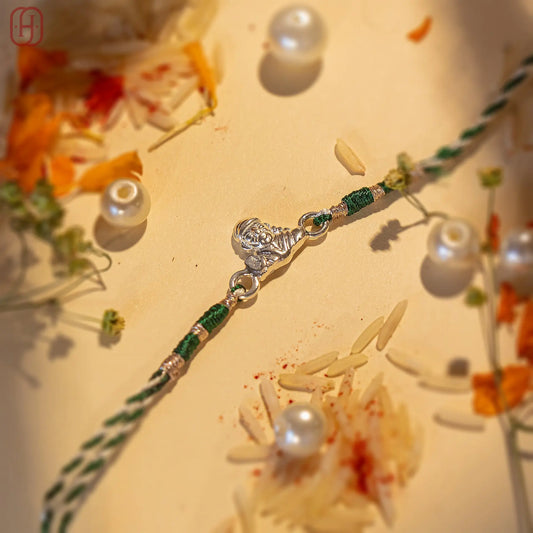 Sai Baba silver rakhi with green and white threads surrounded by flowers and pearls