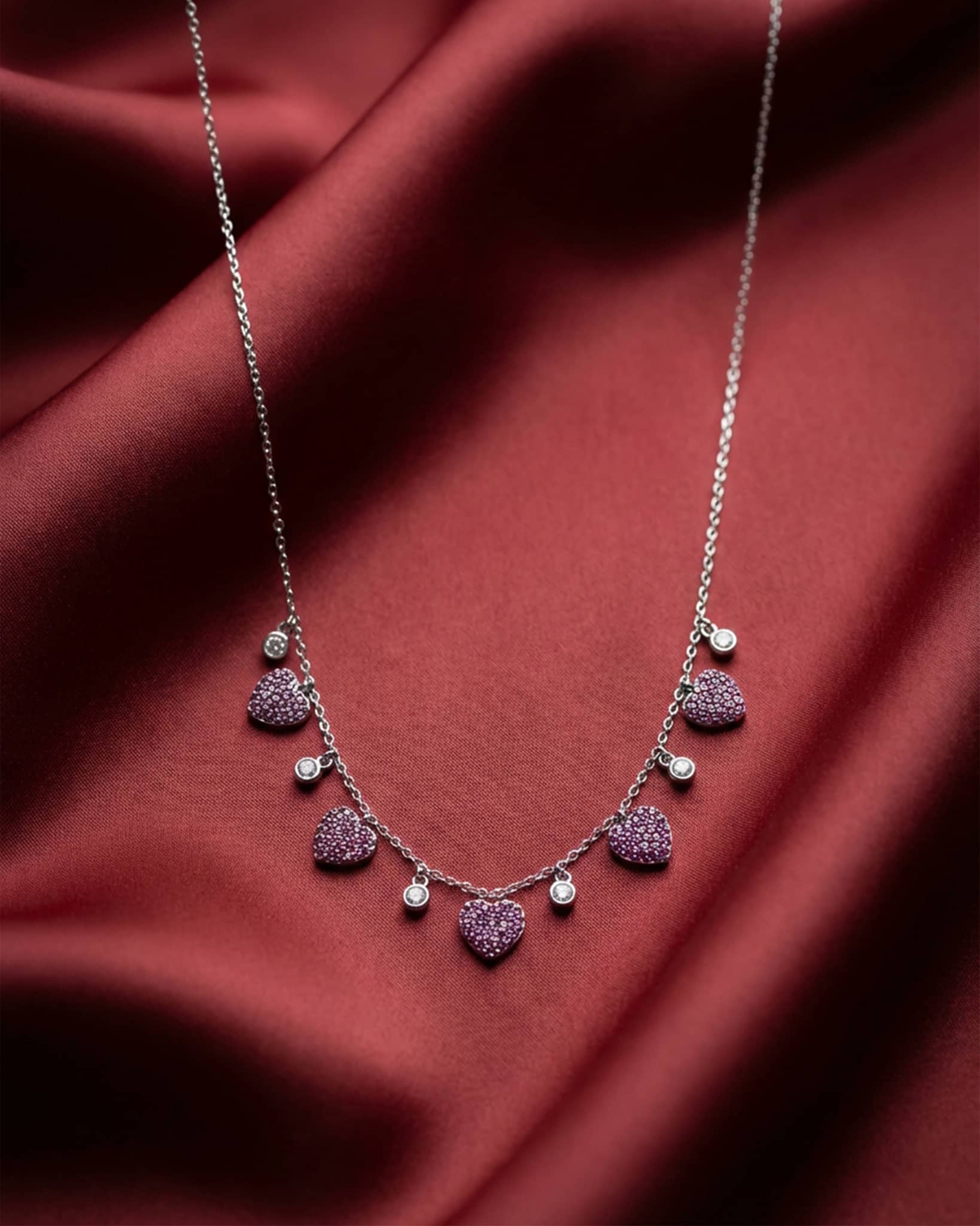 92.5 sterling silver necklace featuring dangling pink pave heart charms and white crystal stations.