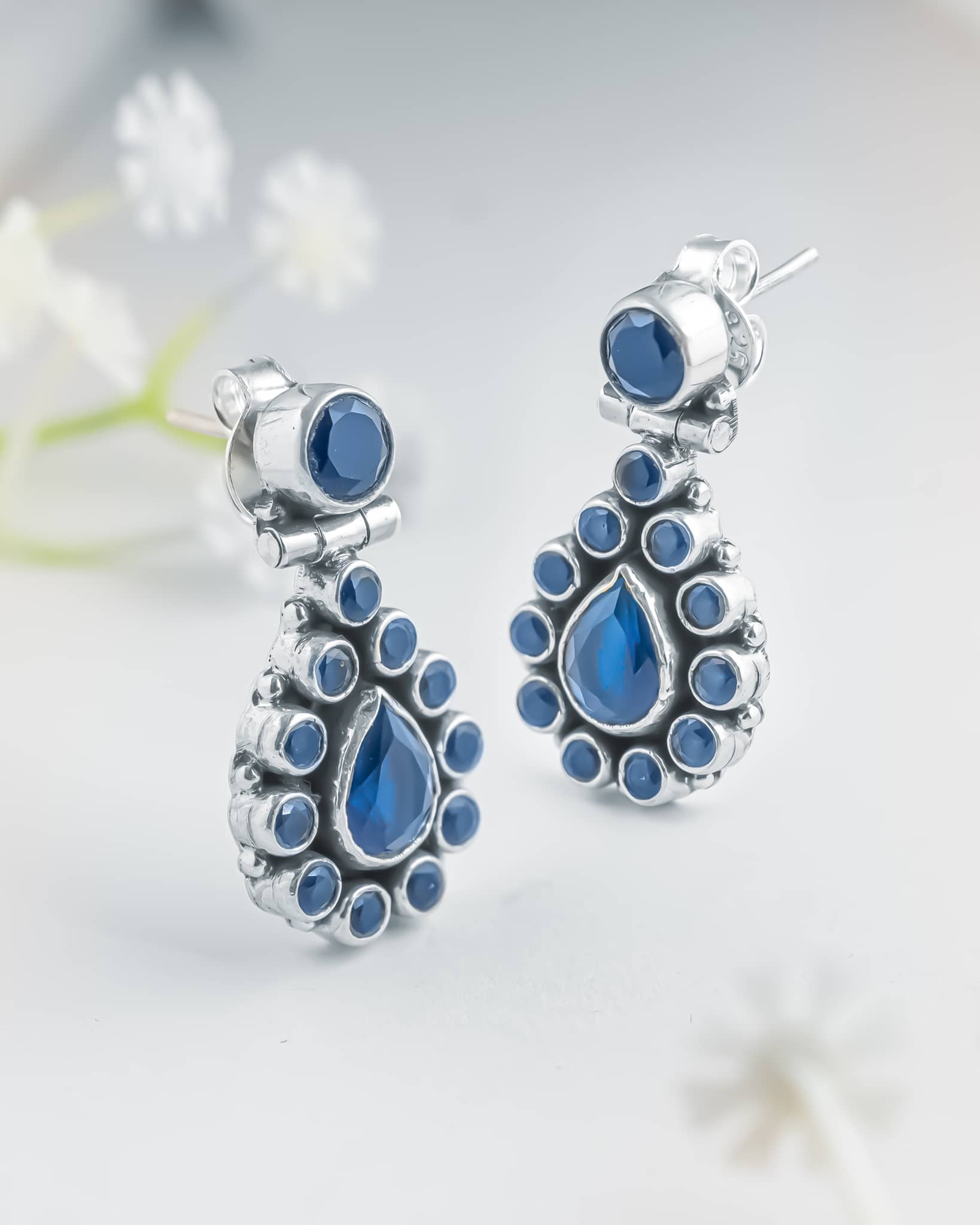 Front and side profile view of silver oxidized drop earrings showcasing a round top stud, a hinged teardrop blue cz halo, and push-back closures