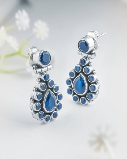 Front and side profile view of silver oxidized drop earrings showcasing a round top stud, a hinged teardrop blue cz halo, and push-back closures