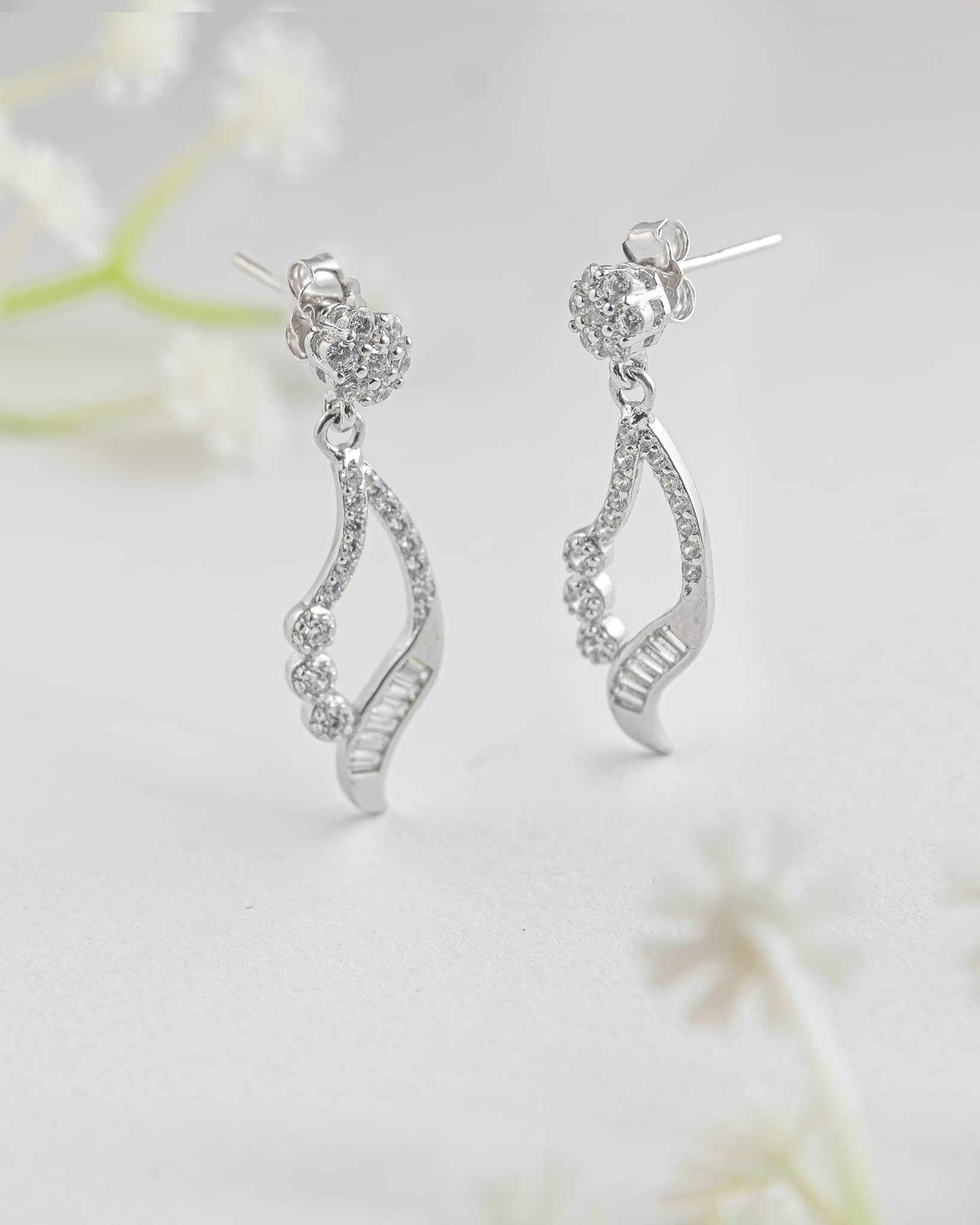 Floating angled shot of elegant 92.5 sterling silver open teardrop dangle earrings featuring a mix of sparkling round and baguette clear cz stones.
