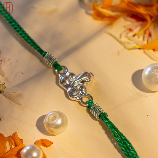 925 silver Ganesh Ji Rakhi with green braided thread and decorative silver accents by Hardik Jewels