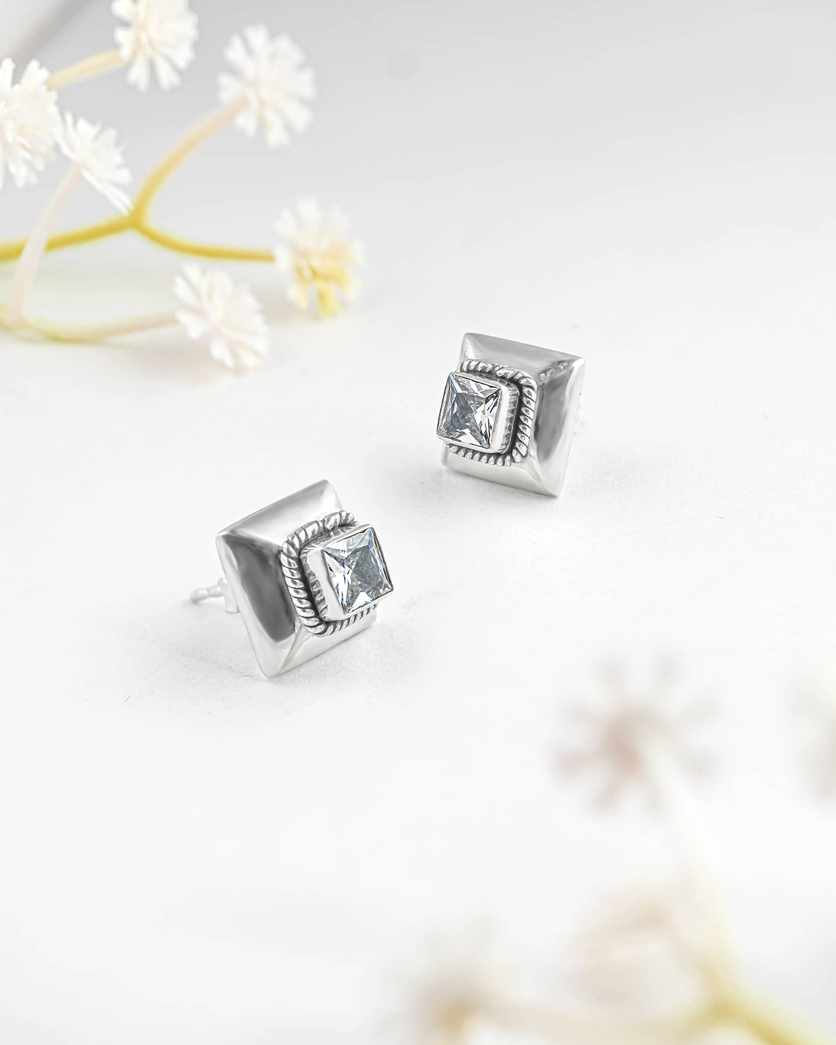 Floating angled shot of modern 92.5 sterling silver square stud earrings highlighting the clear cz stone and textured rope border against a white background.