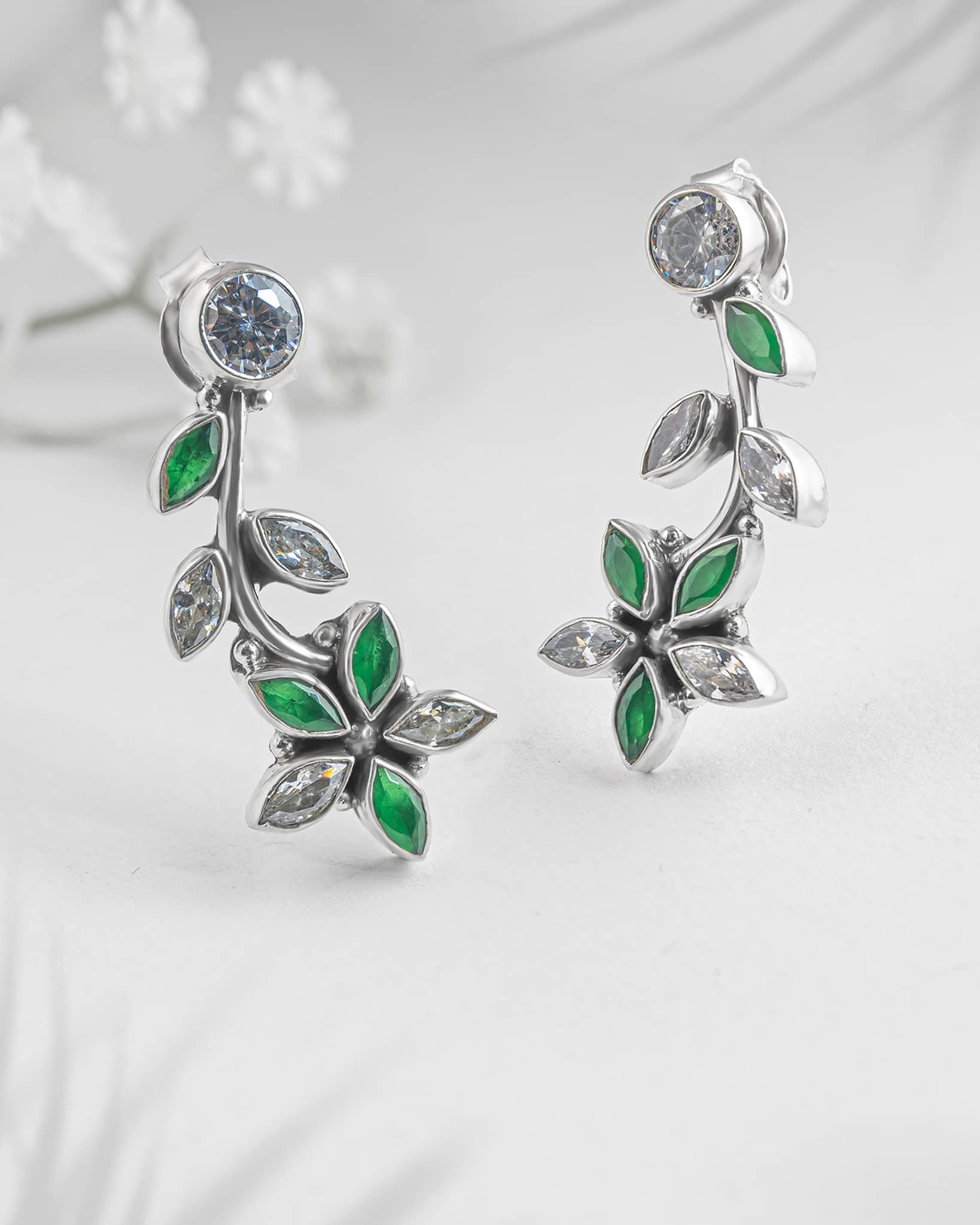 Floating angled shot of elegant 92.5 sterling silver curved drop earrings featuring a nature-inspired vine and flower design with sparkling green and clear cz stones.