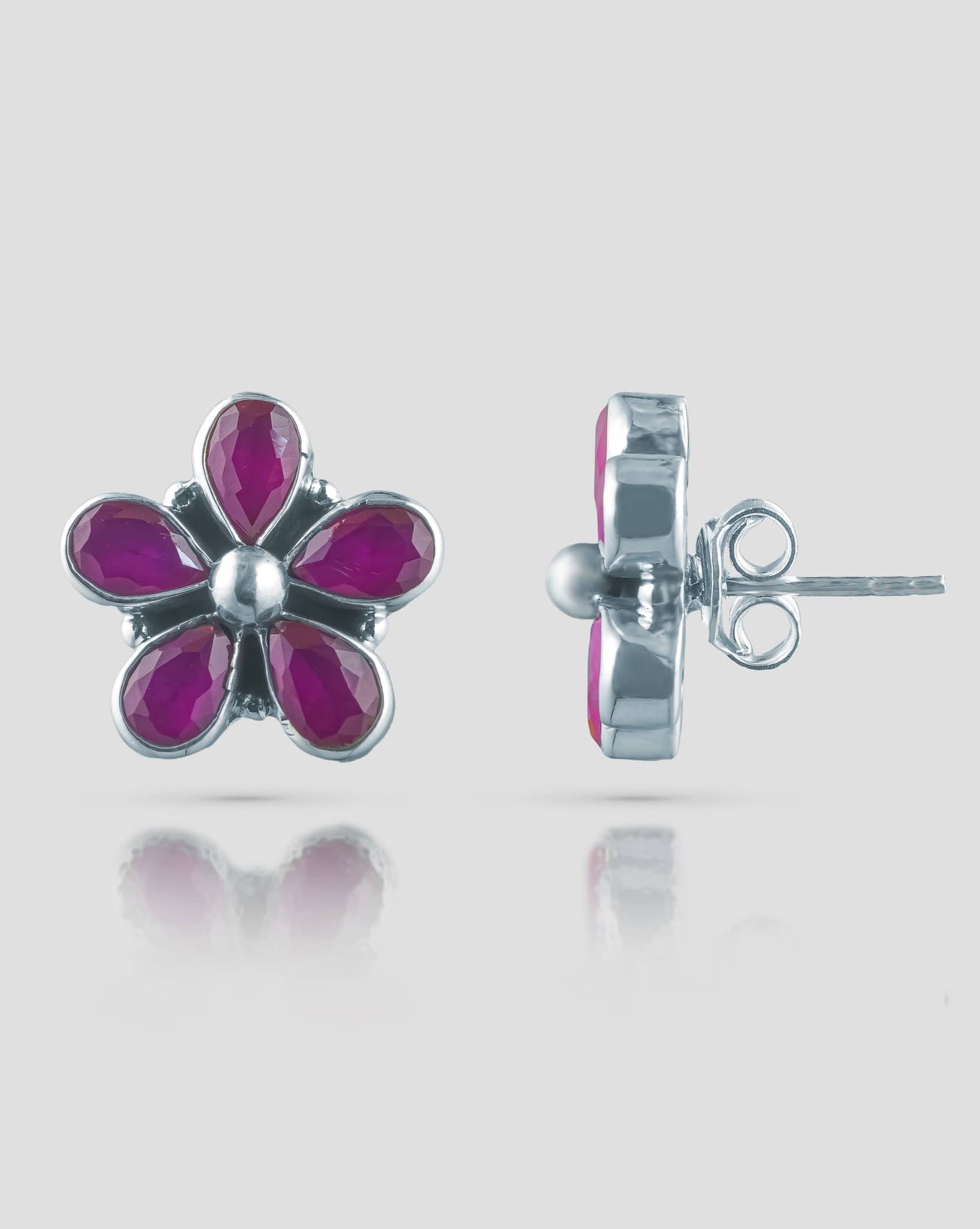 Floating angled shot of cute 92.5 sterling silver 5-petal flower stud earrings highlighting the vibrant ruby pink stones against a white background