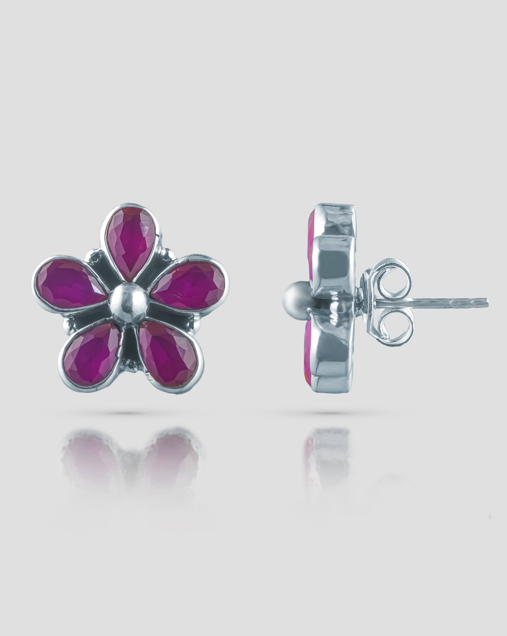 Floating angled shot of cute 92.5 sterling silver 5-petal flower stud earrings highlighting the vibrant ruby pink stones against a white background
