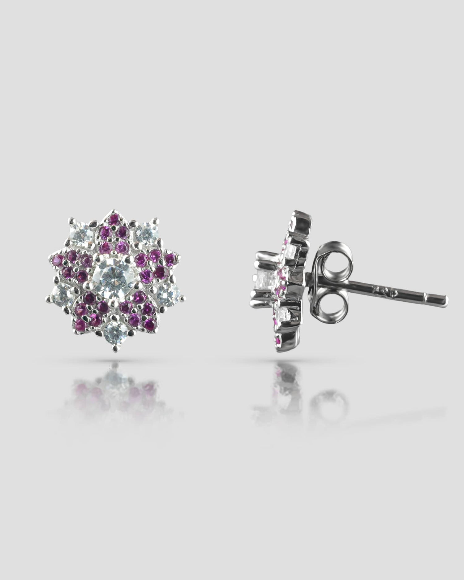 Front and side profile view of silver floral stud earrings showcasing a clear cz center, an inner ruby pink halo, and an outer clear cz petal halo with a push-back closure.