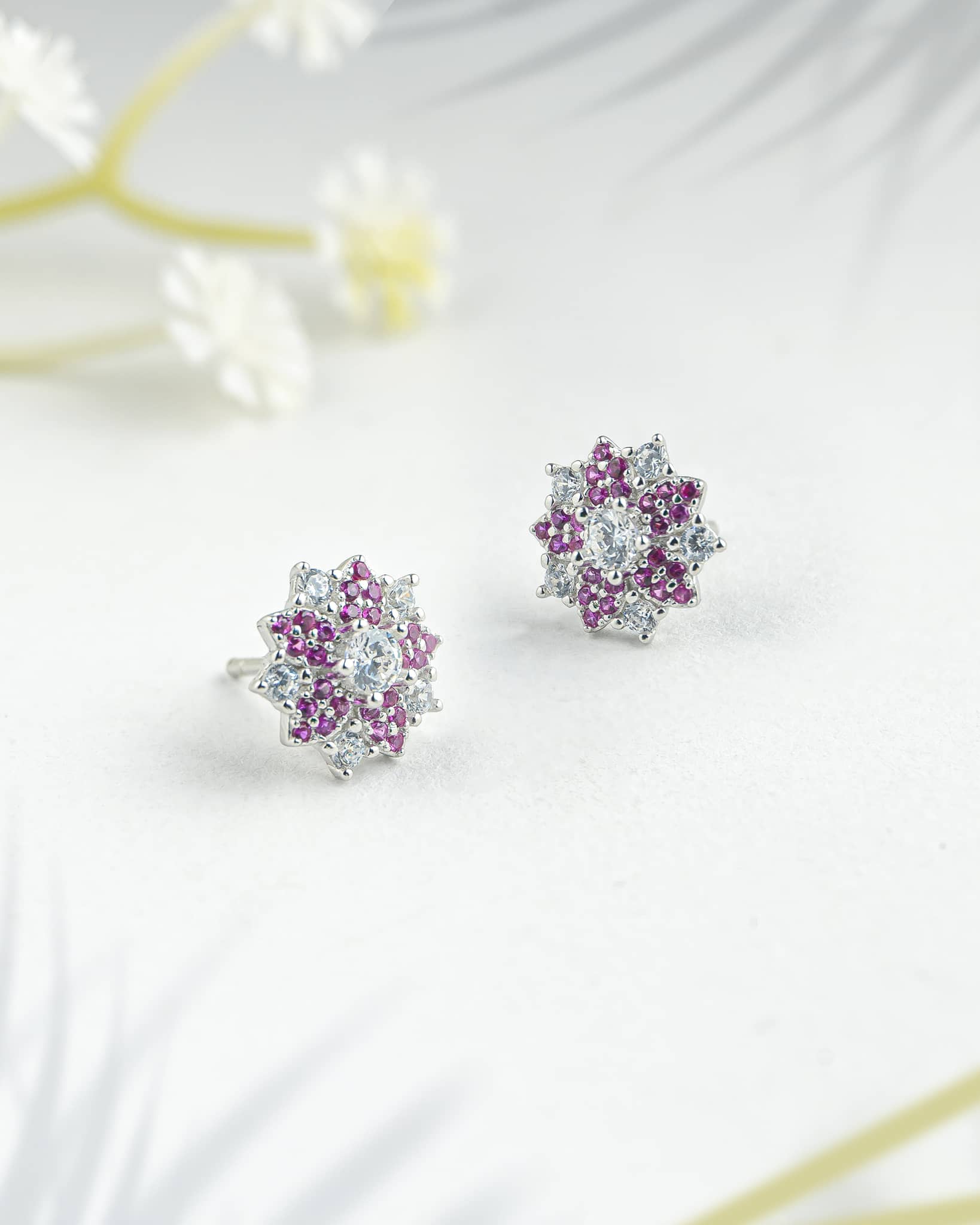 Floating angled shot of elegant 92.5 sterling silver floral stud earrings featuring a vibrant mix of pink and clear cz stones in a sunburst design.