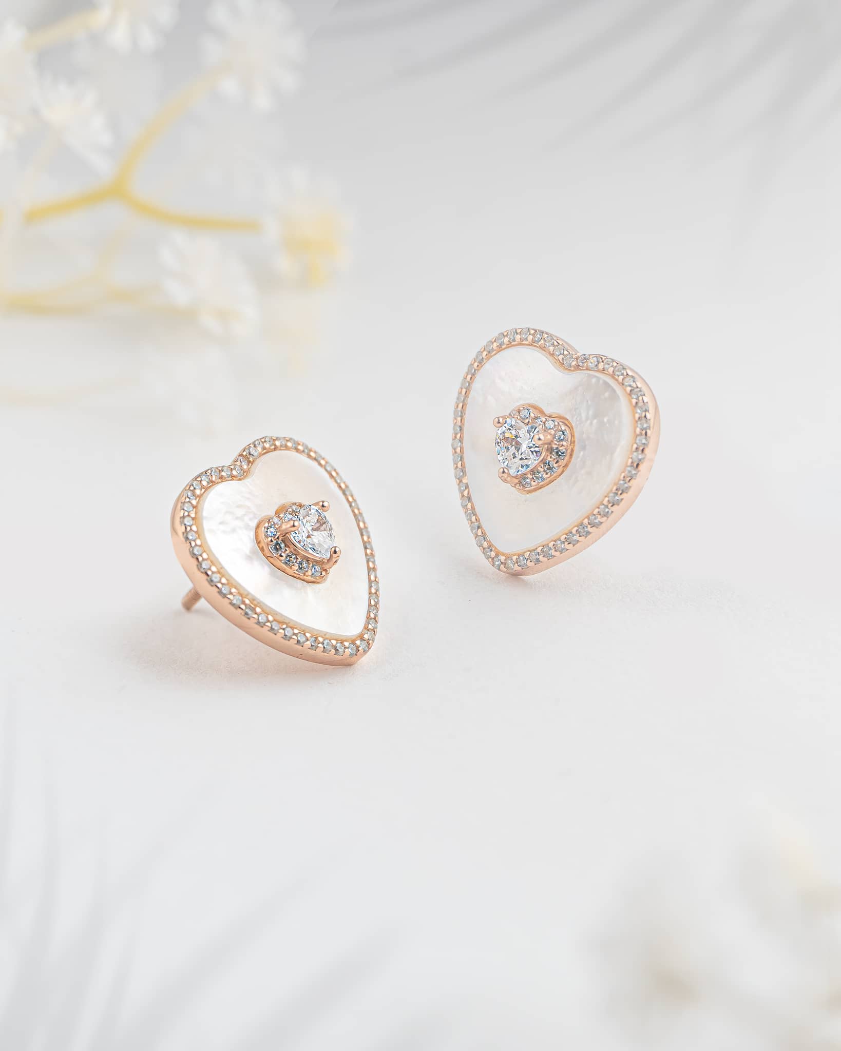 Floating angled shot of elegant 92.5 sterling silver rose gold plated heart stud earrings featuring a luminous white mother of pearl base and sparkling clear cz stones.