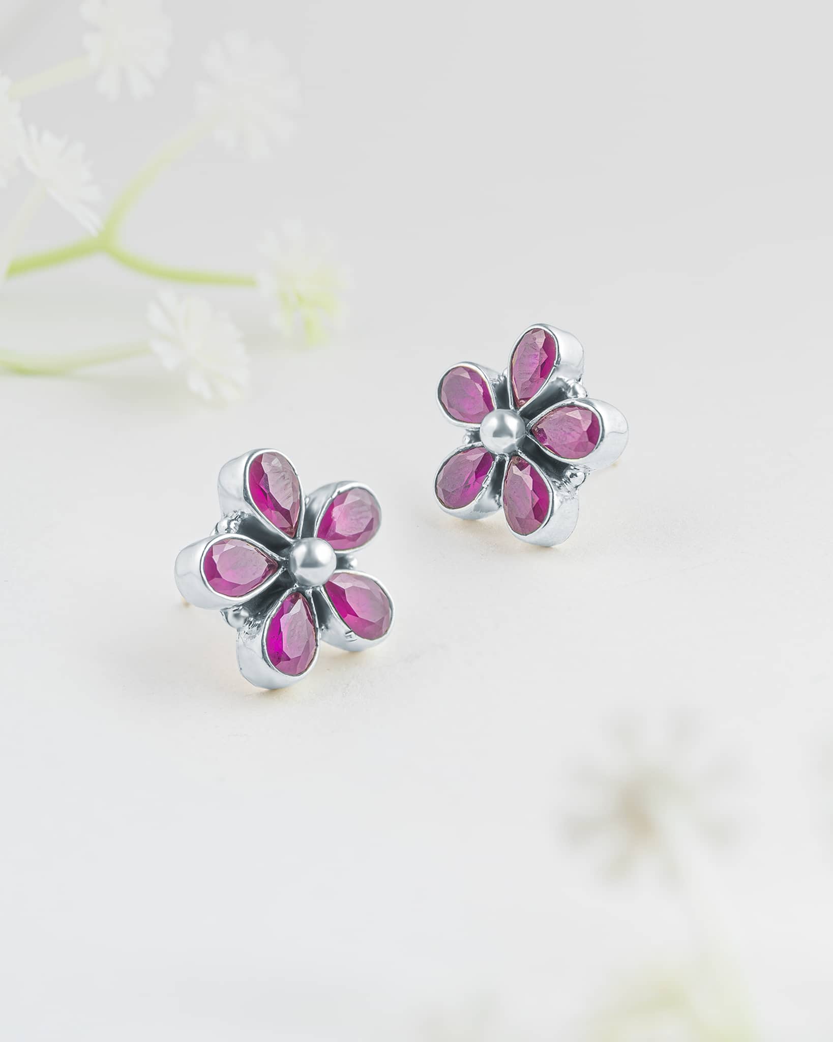 Front and side profile view of silver floral stud earrings showcasing five pear-cut ruby pink stones in bezel settings with a smooth silver center dome and push-back closures