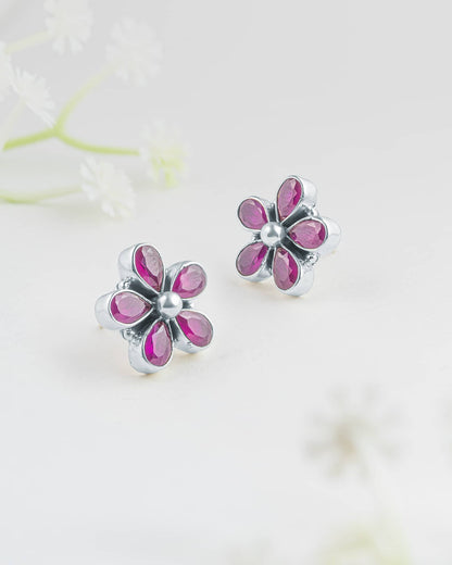 Front and side profile view of silver floral stud earrings showcasing five pear-cut ruby pink stones in bezel settings with a smooth silver center dome and push-back closures