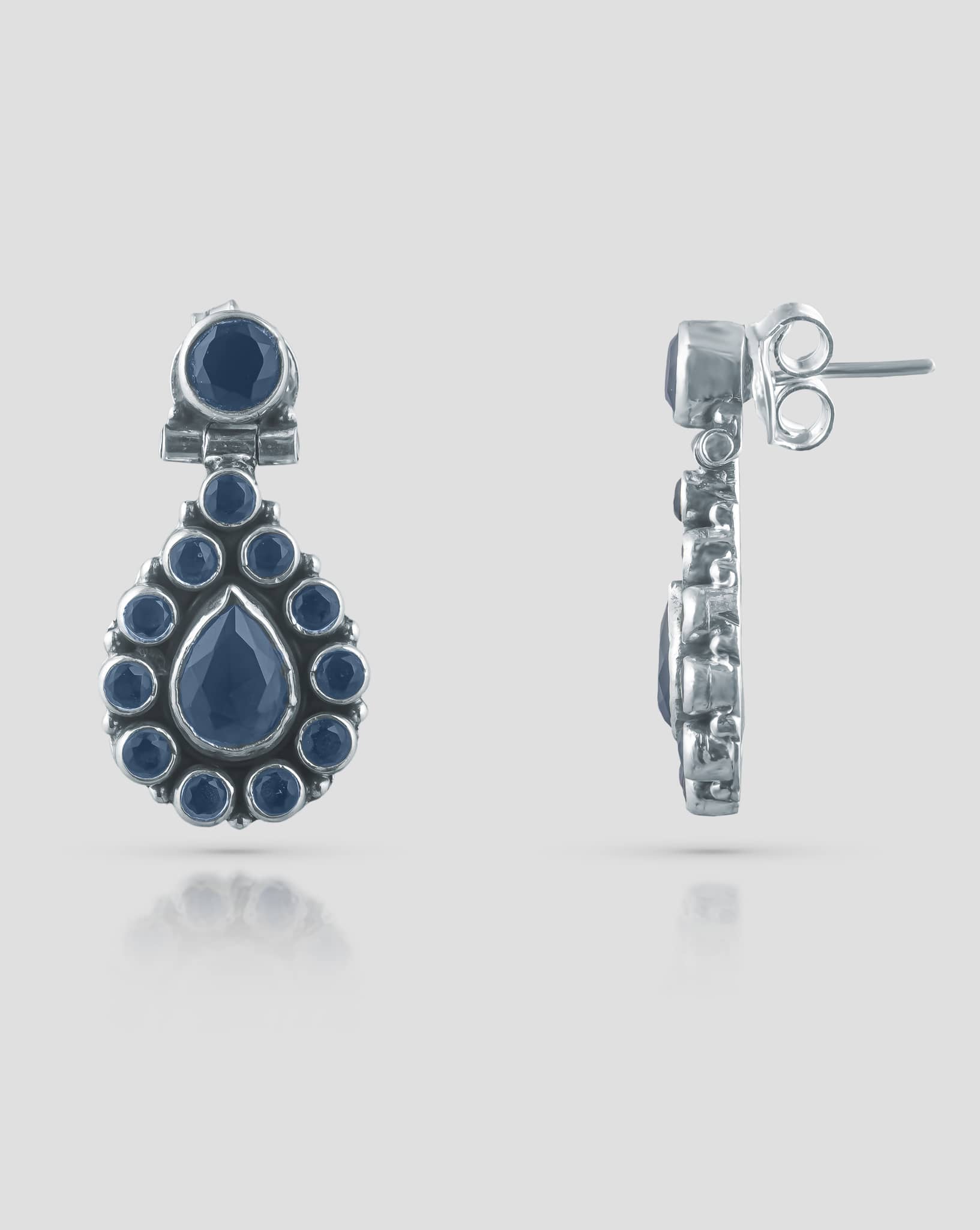 Floating angled shot of royal 92.5 sterling silver antique drop earrings featuring deep blue cz stones in a teardrop halo design