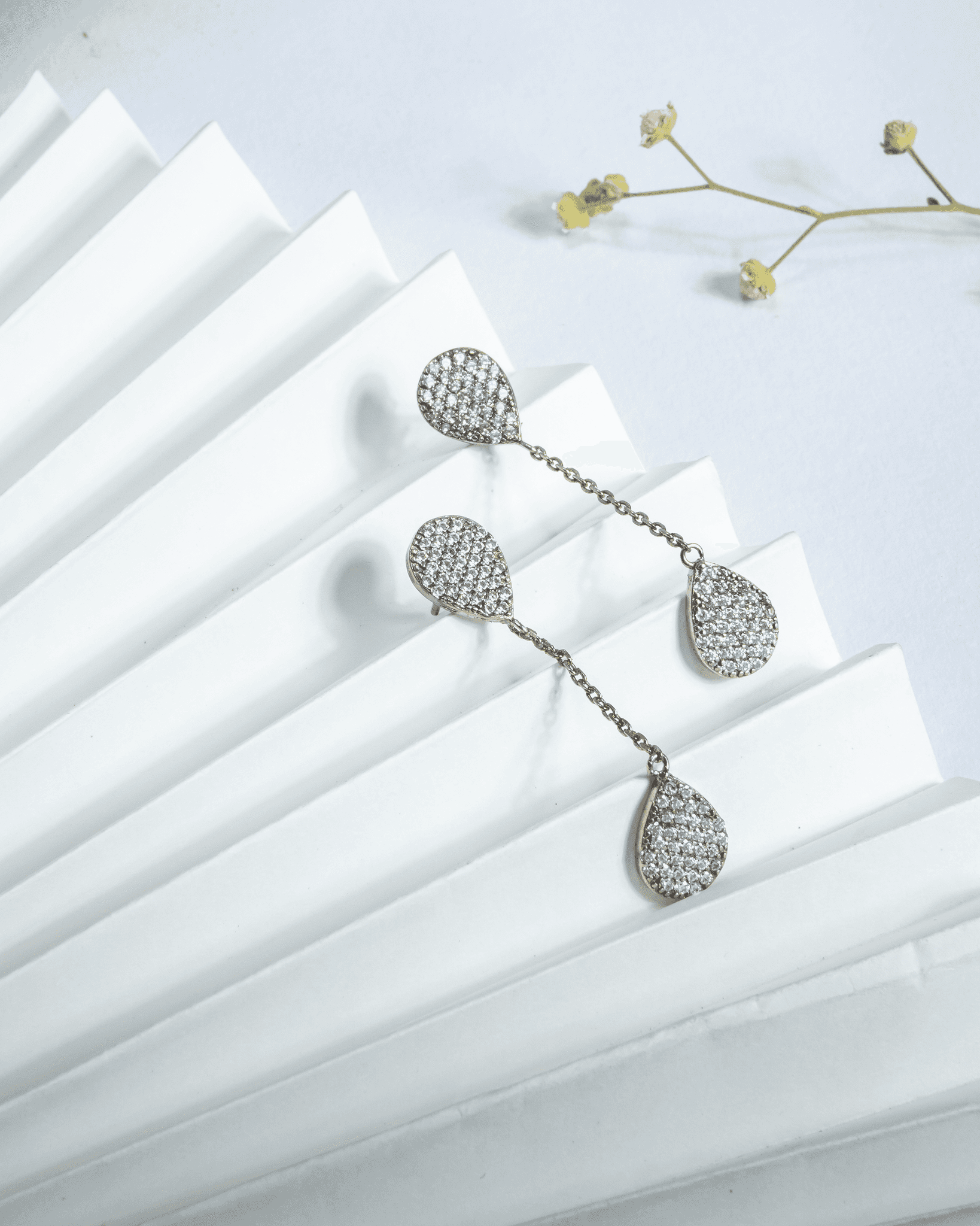 925 sterling silver double teardrop dangler earrings paved with white american diamonds connected by a chain.