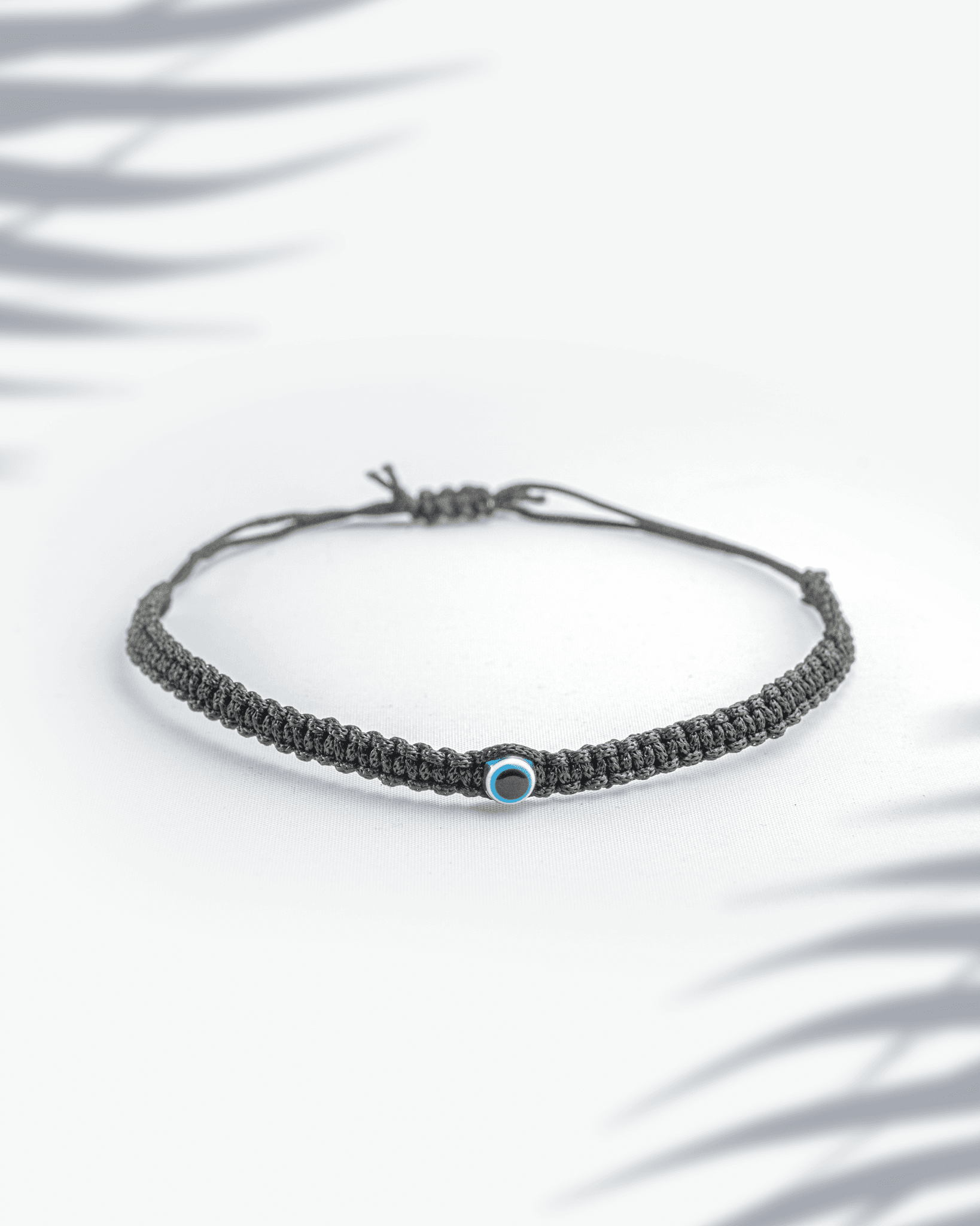 Black thread woven bracelet featuring a small blue evil eye bead with adjustable sliding knot.