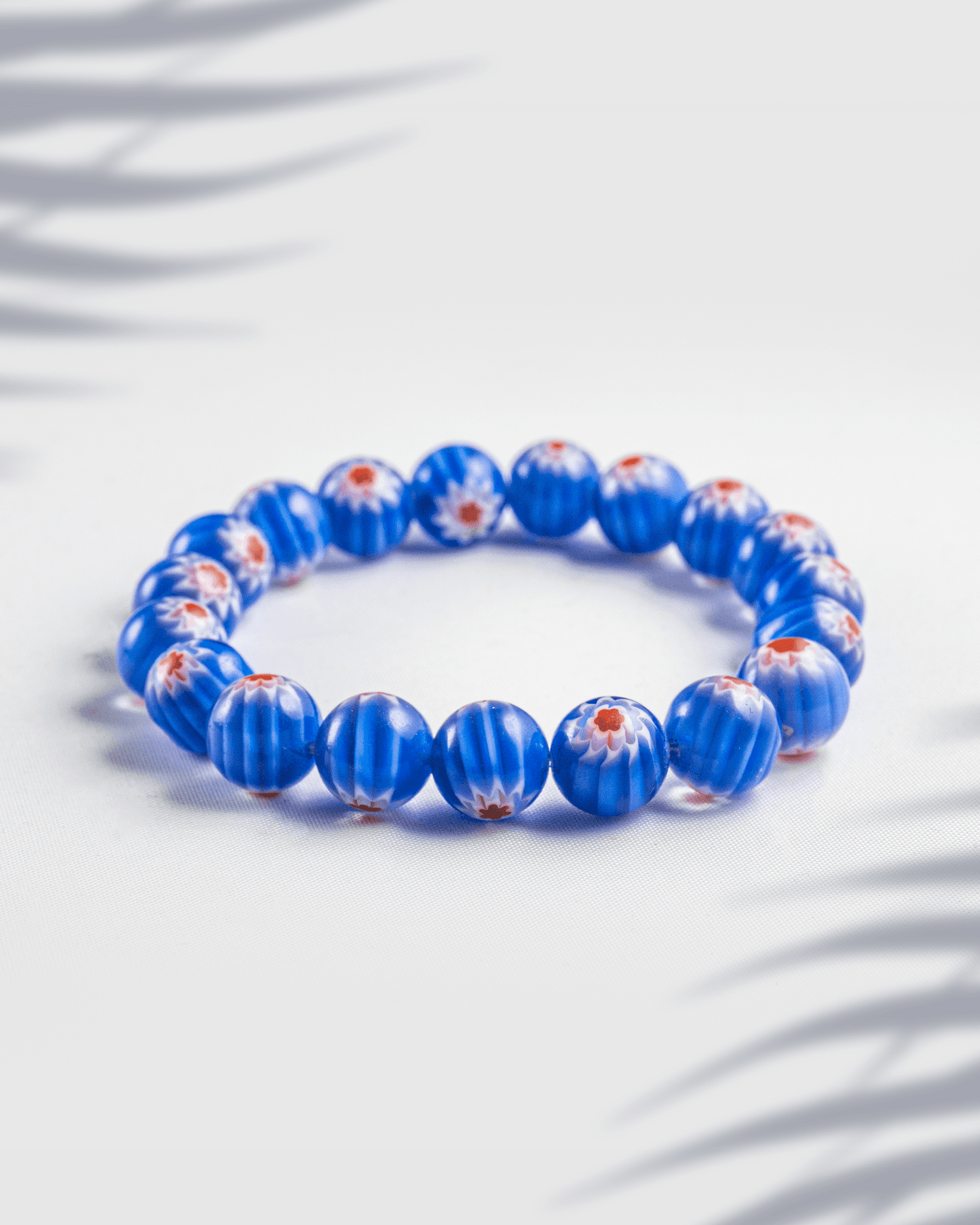Blue beaded bracelet featuring ribbed beads with red and white floral millefiori patterns on a white background.