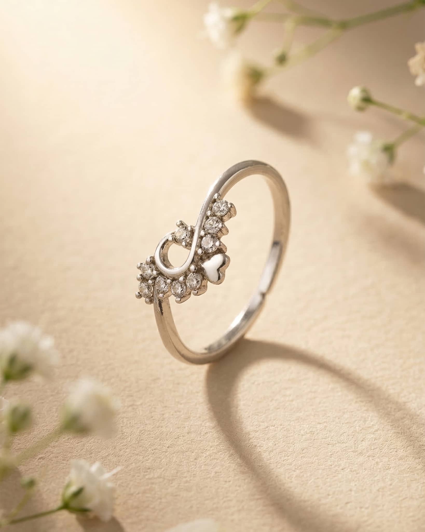 Close up of a delicate silver promise ring resting on a textured surface, showing an infinity inspired design with clear cz stones and a heart motif.