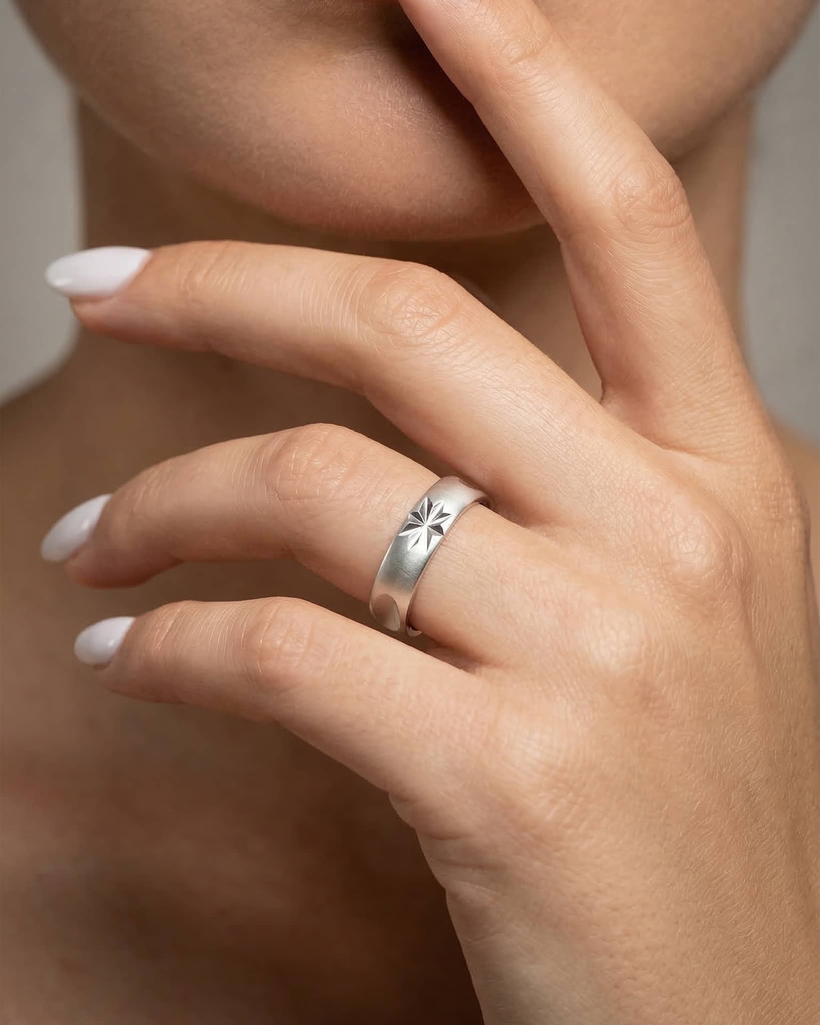Close up of a minimalist 92.5 sterling silver band ring with a matte finish and a bright starburst engraving catching the light.