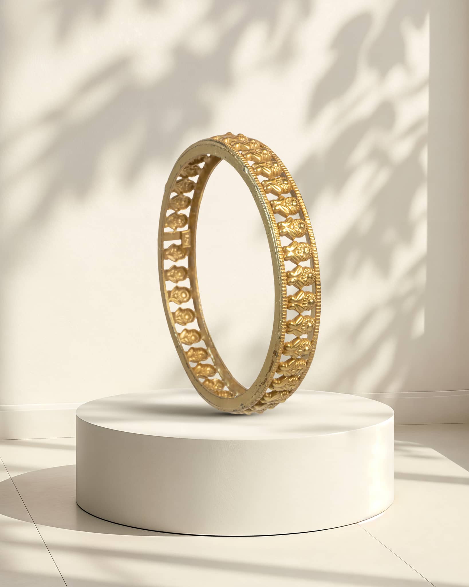 Gold bangle on a white pedestal with a light background