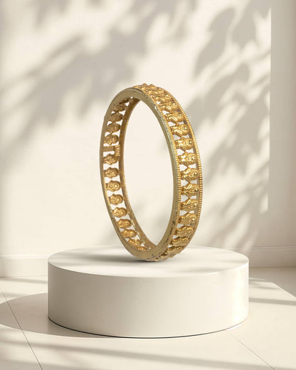 Gold bangle on a white pedestal with a light background