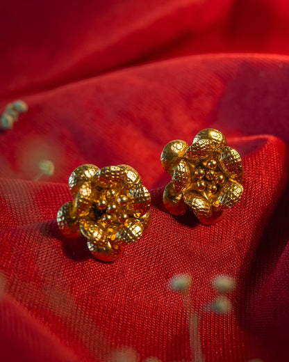 Gold plated 3D floral stud earrings featuring textured hammered petals and a beaded center.