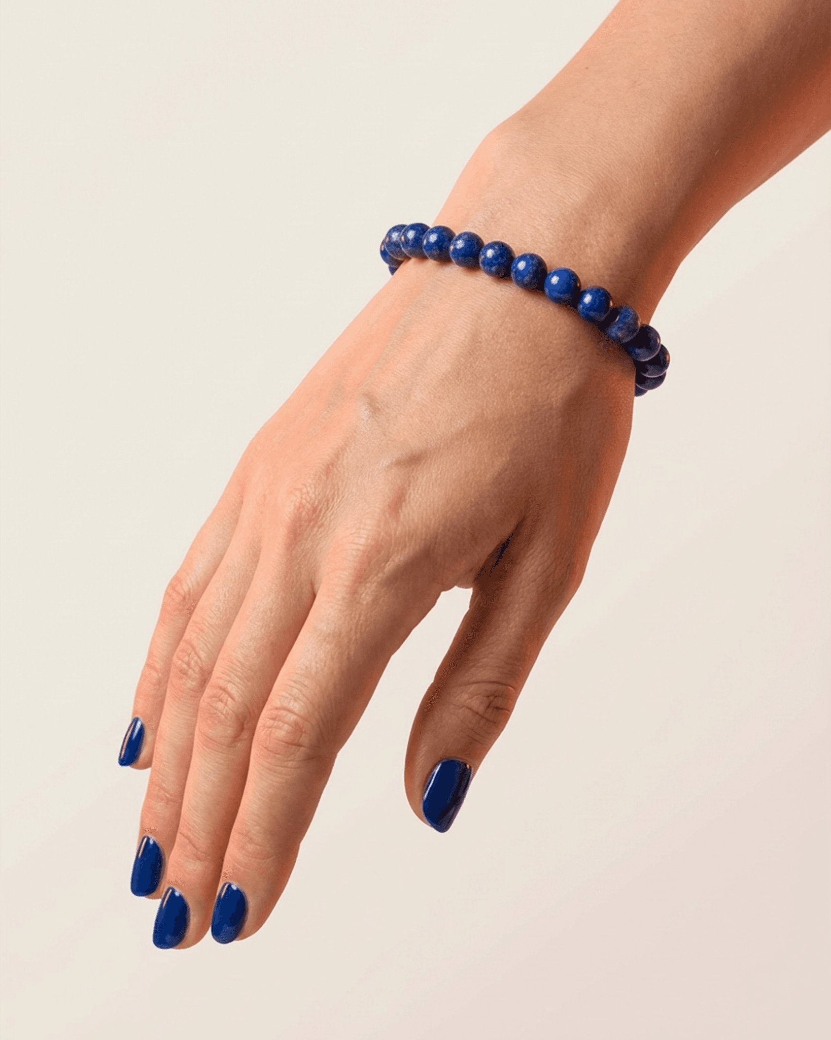 Hand wearing a blue beaded bracelet on a plain background