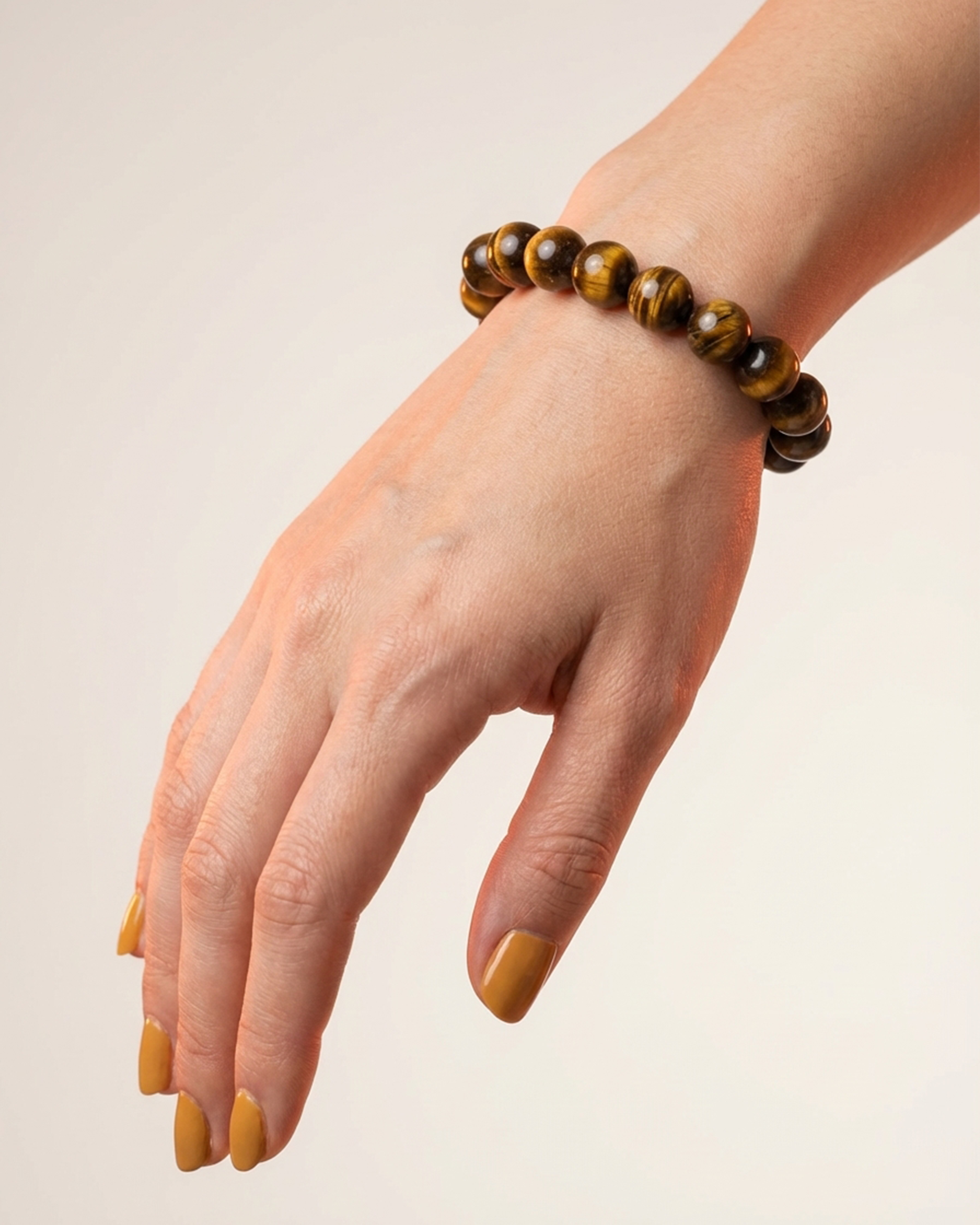 Hand wearing a tiger's eye bracelet on a plain background