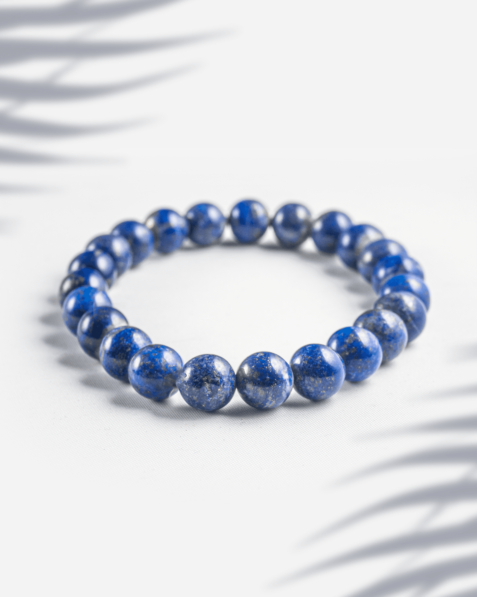 Natural Lapis Lazuli gemstone bracelet featuring deep blue beads with golden pyrite specks on a white background.