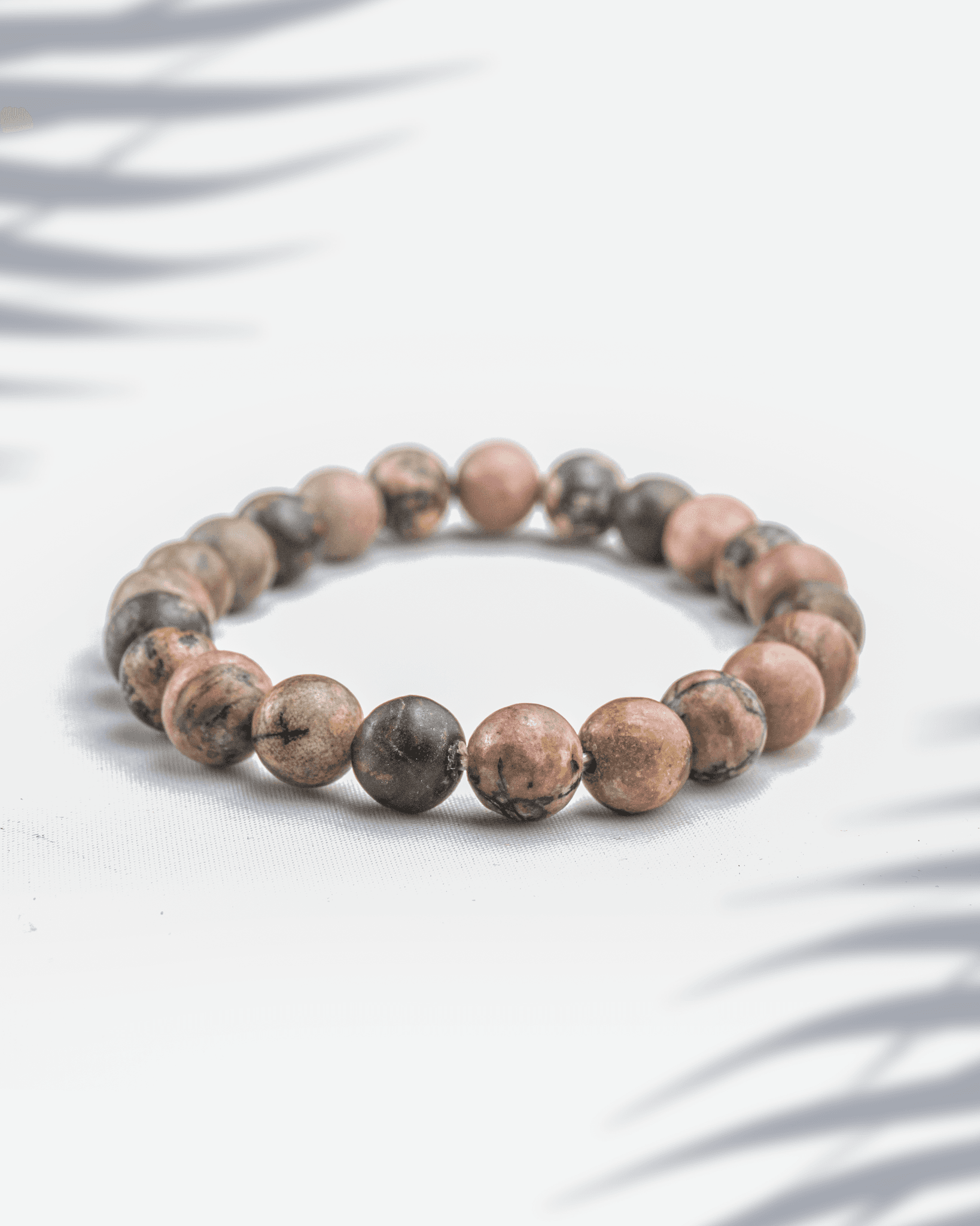Natural Rhodonite gemstone bracelet featuring pink beads with black veins on a white background.