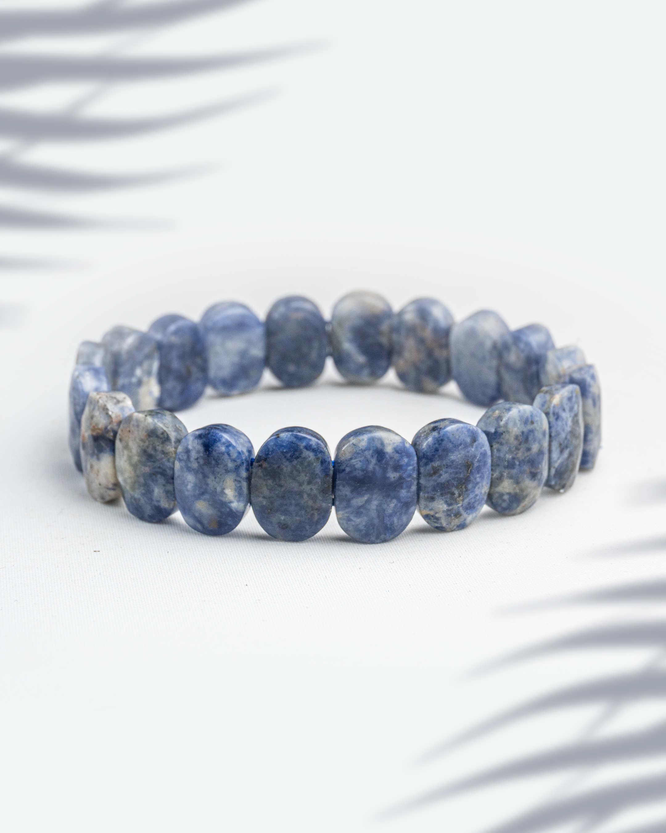 Natural blue sodalite gemstone bracelet featuring flat oval tablet beads with white veins on a white background.