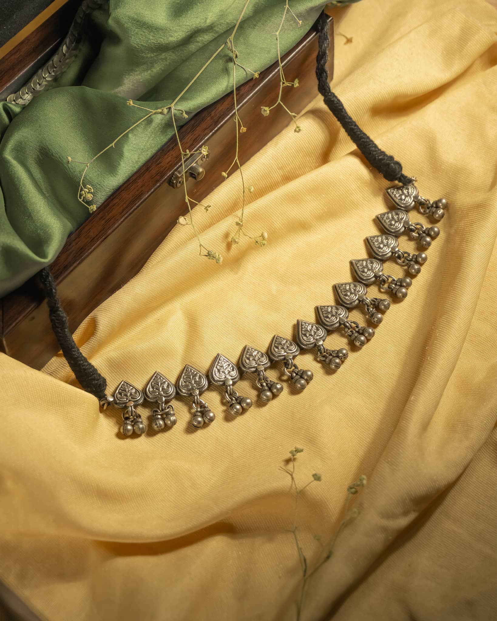 Oxidized 925 sterling silver heart motif choker necklace with ghungroos strung on a black thread, displayed on a yellow background.