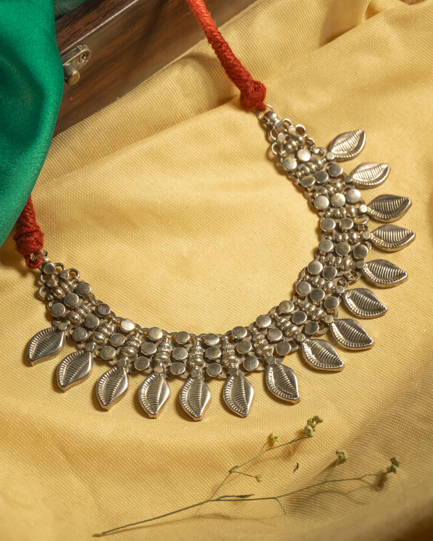 Oxidized 925 sterling silver leaf motif choker necklace strung on a vibrant red thread, displayed on a yellow background.
