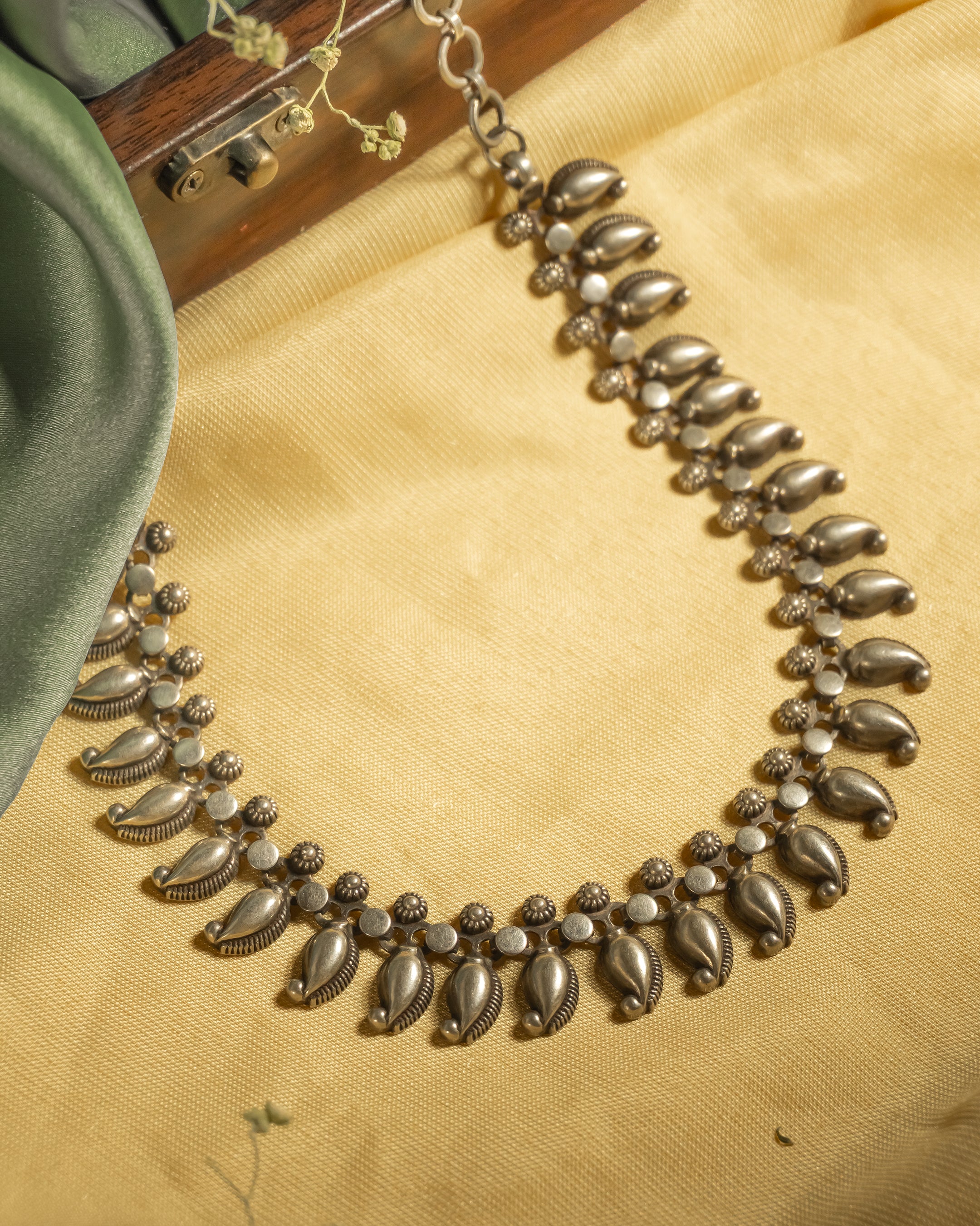 Oxidized 925 sterling silver necklace featuring repeating mango (paisley) motifs linked together, displayed on a yellow background.