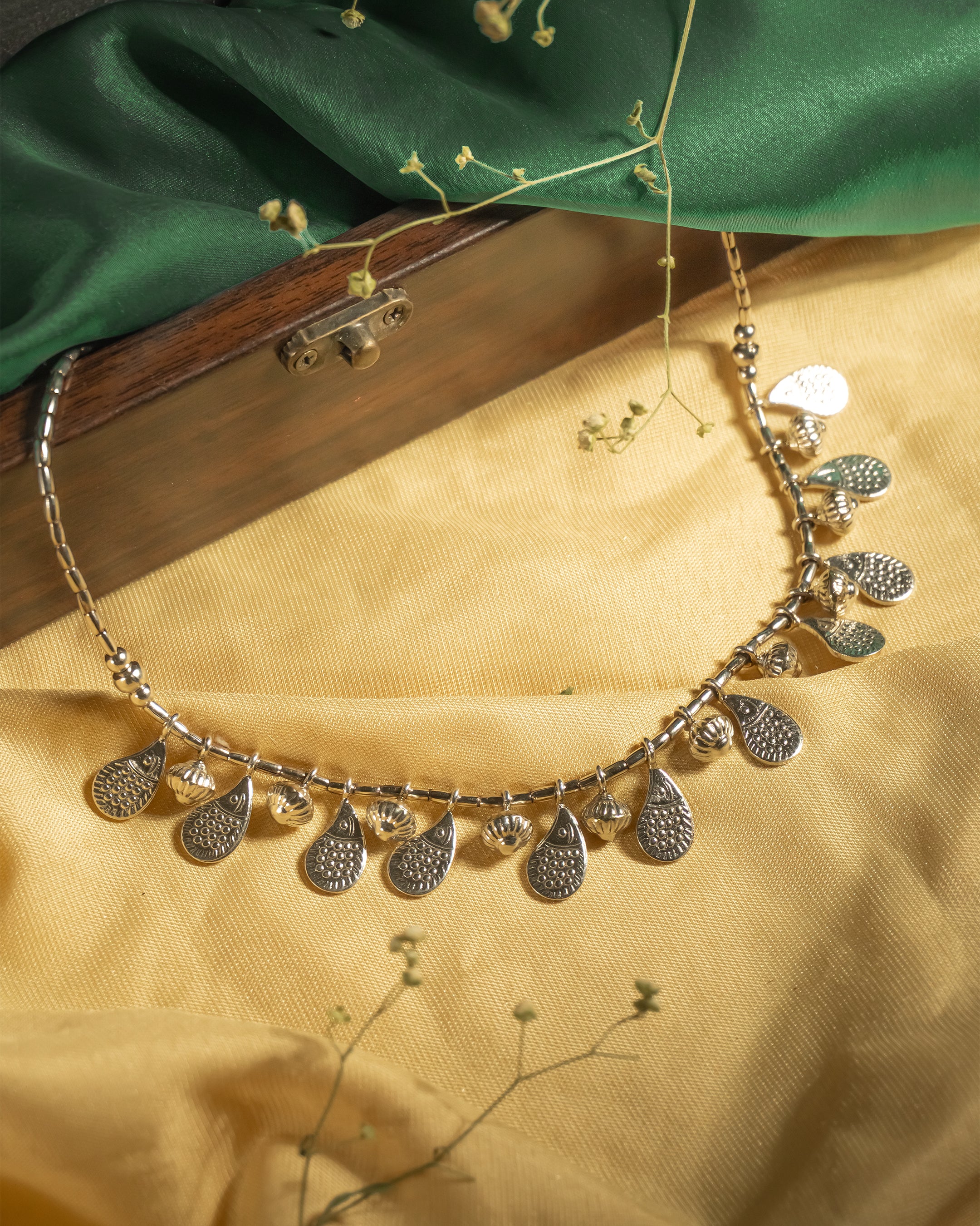 Oxidized 925 sterling silver necklace with cylindrical beads and dangling textured teardrop charms, displayed on a yellow background.