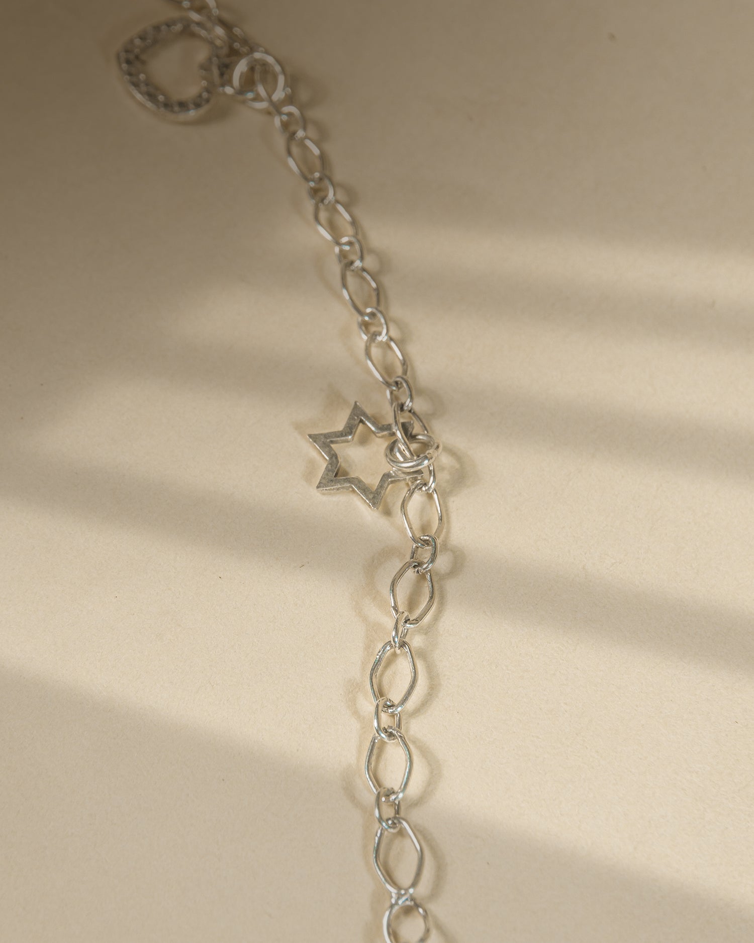 Pair of 925 sterling silver chain anklets featuring dangling heart and star charms on a beige background.