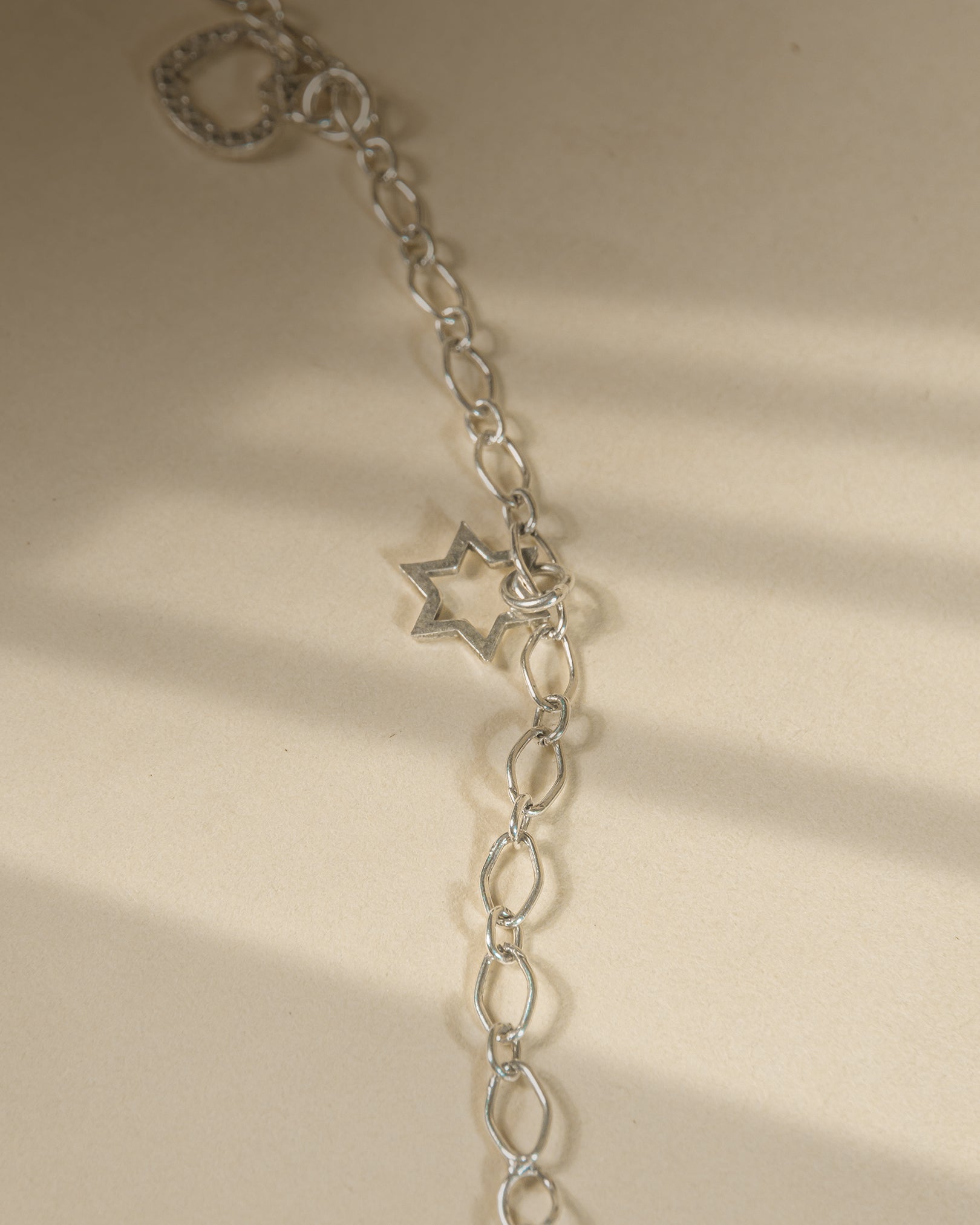 Pair of 925 sterling silver chain anklets featuring dangling heart and star charms on a beige background.