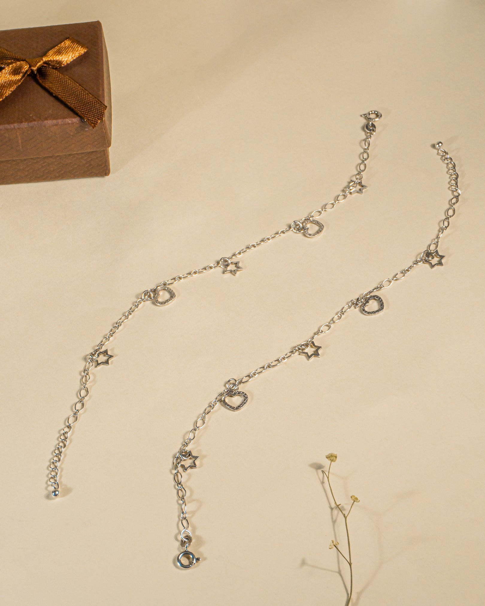 Pair of 925 sterling silver chain anklets featuring dangling heart and star charms on a beige background.