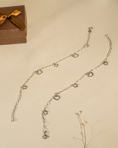 Pair of 925 sterling silver chain anklets featuring dangling heart and star charms on a beige background.