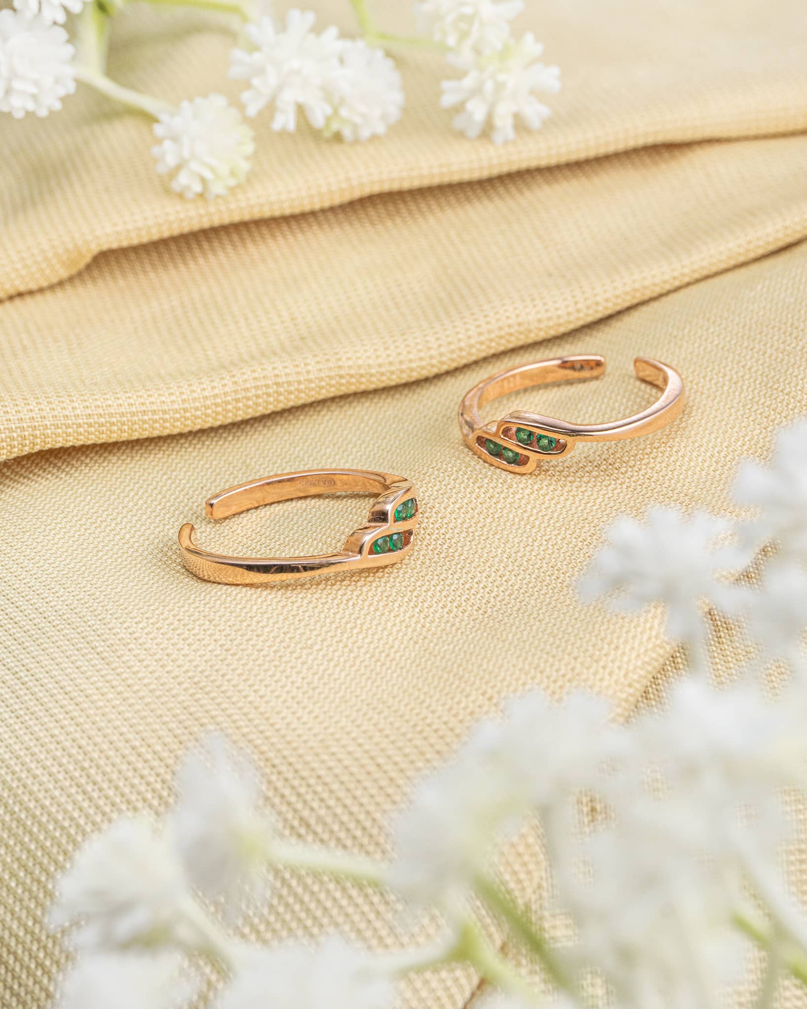 Pair of rose gold plated 92.5 sterling silver adjustable toe rings featuring green stones in a wave design.