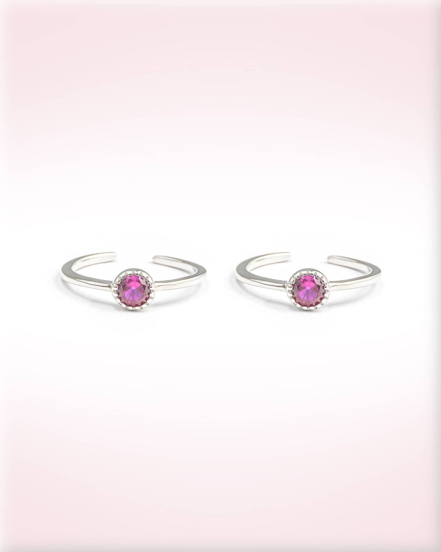 Pair of silver open rings with pink gemstones on a light pink background