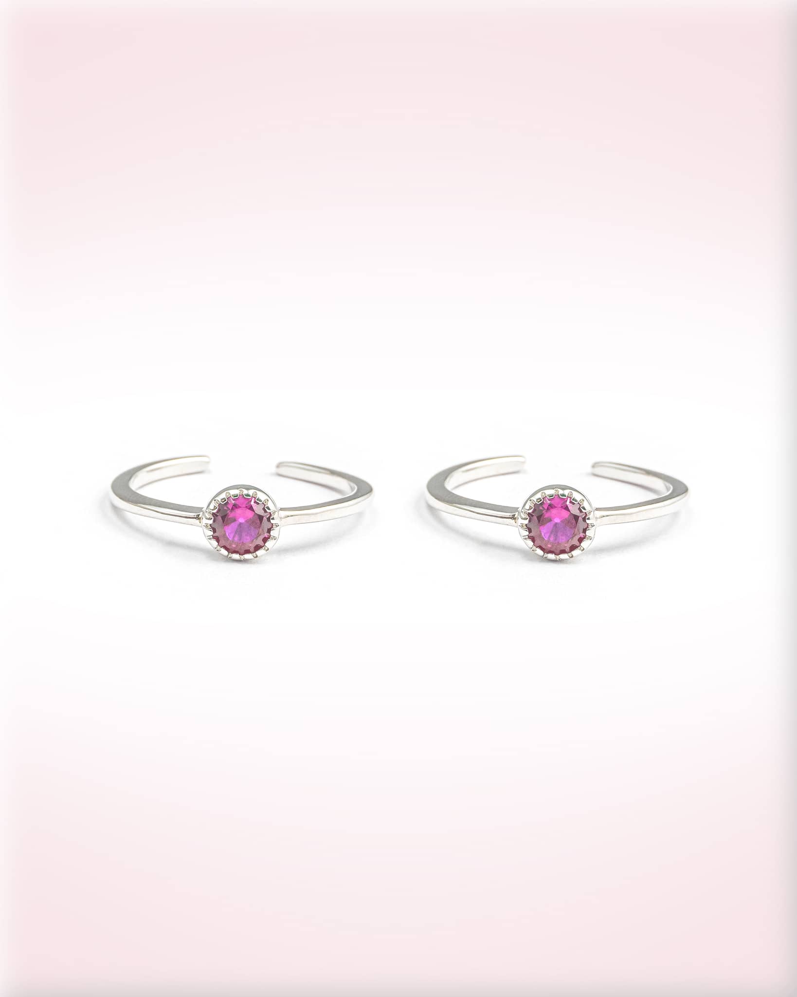 Pair of silver open rings with pink gemstones on a light pink background