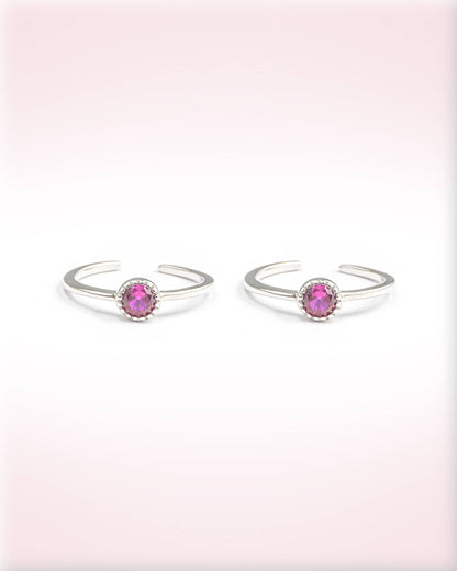 Pair of silver open rings with pink gemstones on a light pink background