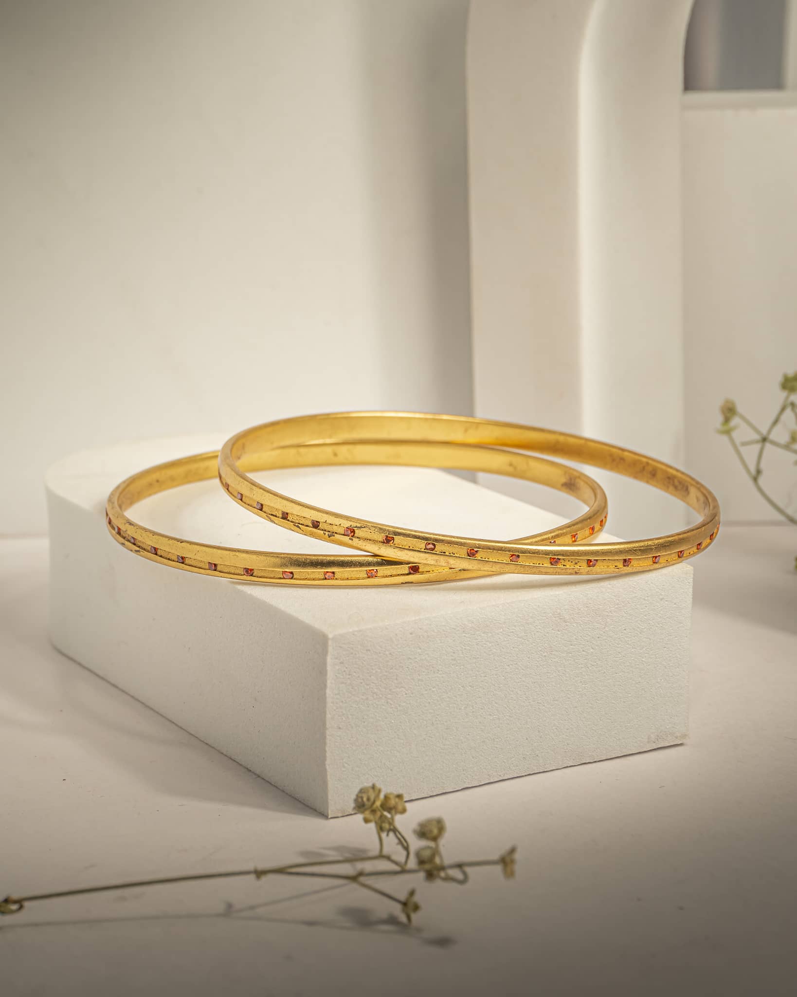 Pair of sleek gold plated 925 sterling silver bangles studded with small red stones on a white block.