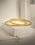 Pair of sleek gold plated 925 sterling silver bangles studded with small red stones on a white block.