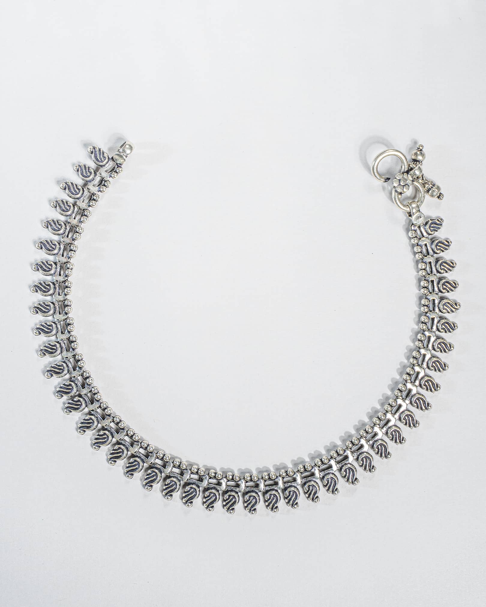 Pair of traditional oxidized silver anklets featuring repeating paisley mango motifs and small silver beads Full details