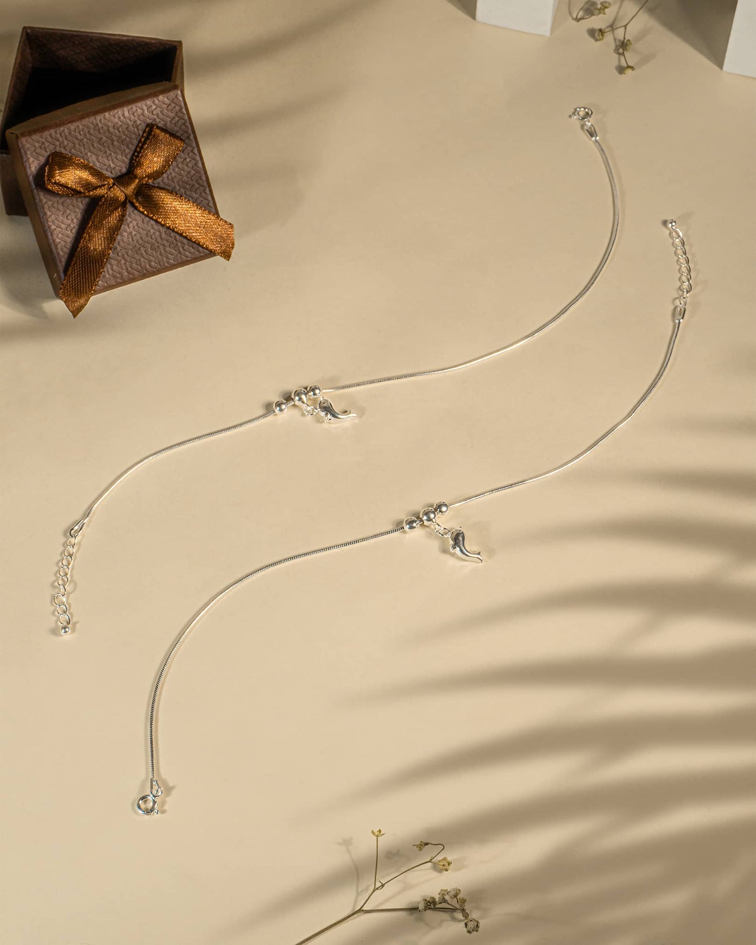 Silver necklace with pendants on a beige surface next to a brown gift box with a bow.