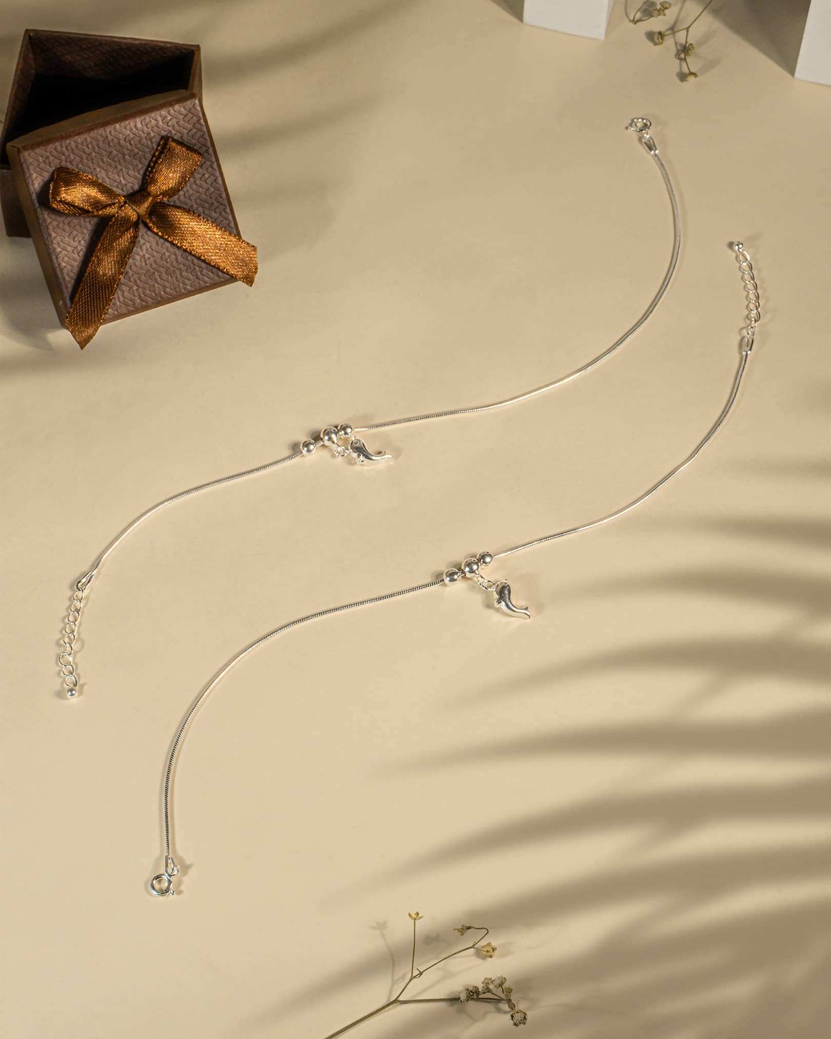 Silver necklace with pendants on a beige surface next to a brown gift box with a bow.