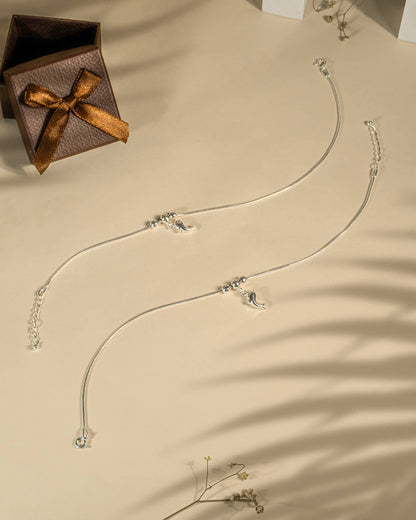 Silver necklace with pendants on a beige surface next to a brown gift box with a bow.