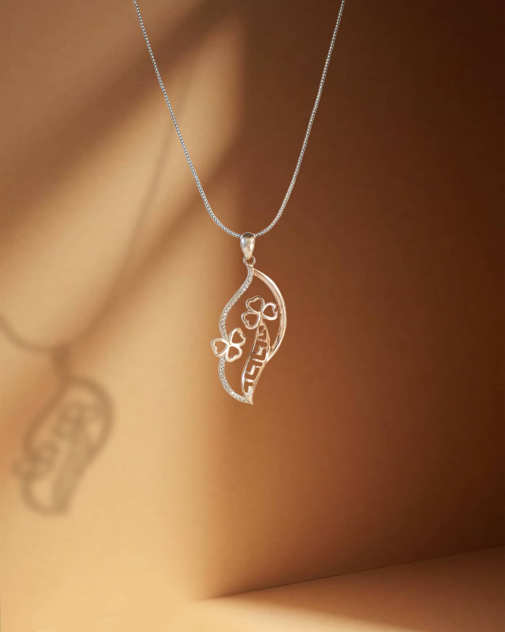 Silver pendanst with a leaf-shaped pendant on a brown background