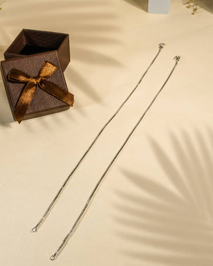 Silver chain necklace on a beige surface with an open brown gift box featuring a bow.
