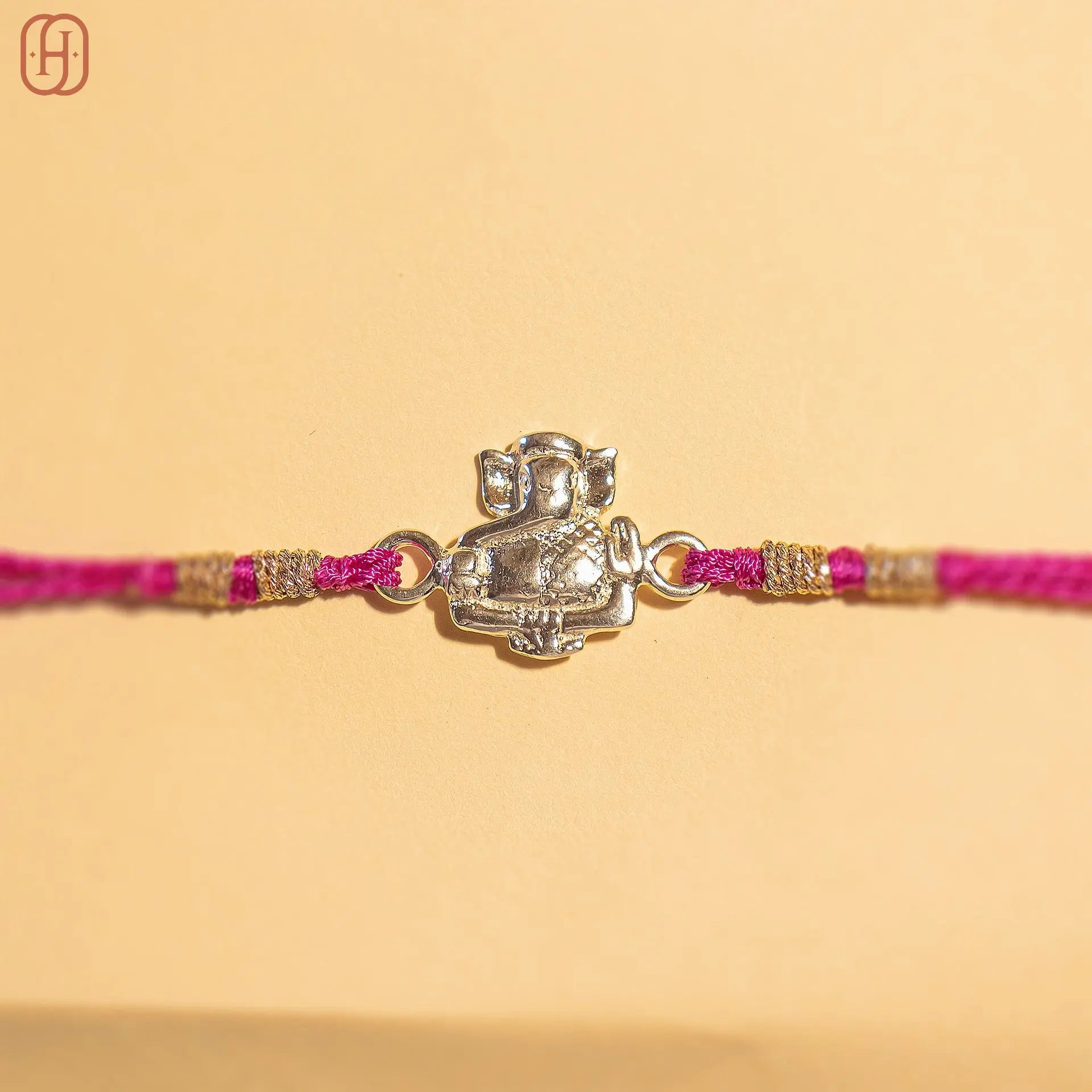 Ganesh Ji face rakhi in silver with pink thread and gold accents from Hardik Jewels